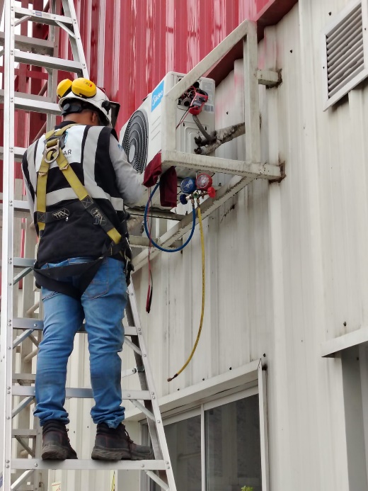 Técnico con arnés realizando mantenimiento de unidad condensadora en altura
